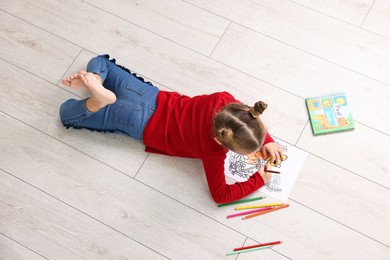 Photo of Cute little girl coloring on warm floor indoors, top view. Heating system