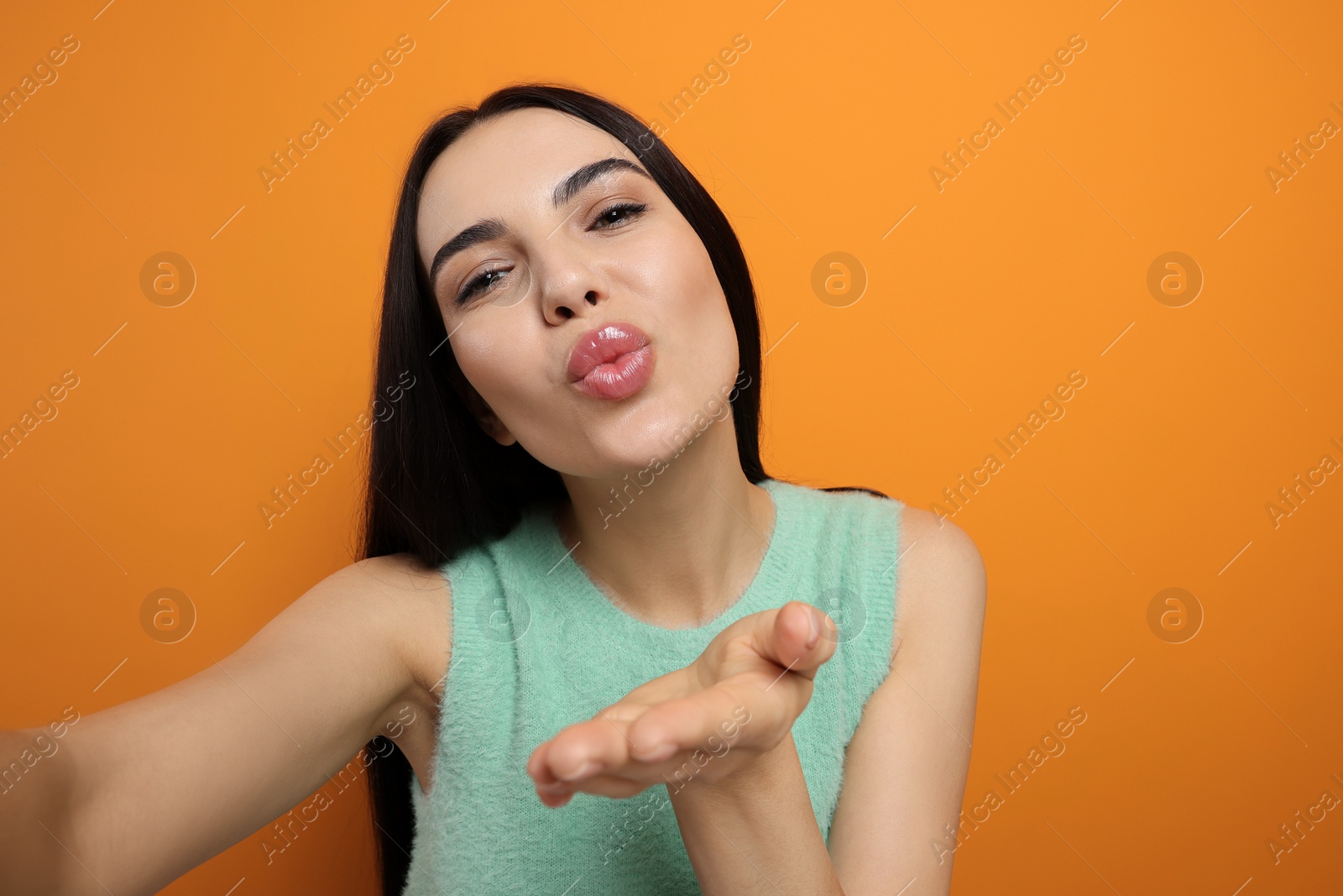 Photo of Beautiful young woman taking selfie while blowing kiss on orange background