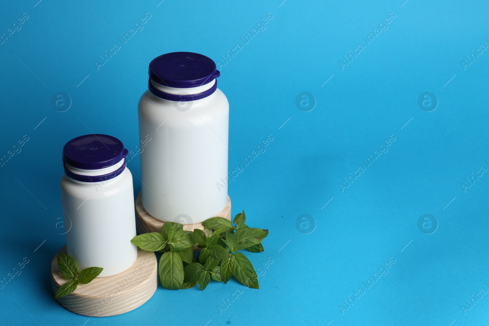 Photo of White medical bottles and mint on light blue background, space for text