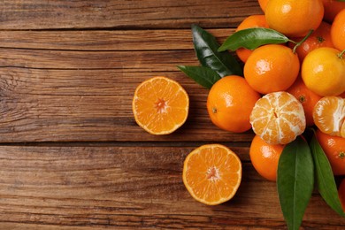 Fresh tangerines with green leaves on wooden table, top view. Space for text