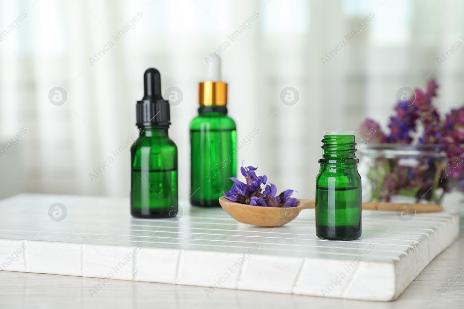 Photo of Bottles of essential oil and sage flowers on table, space for text