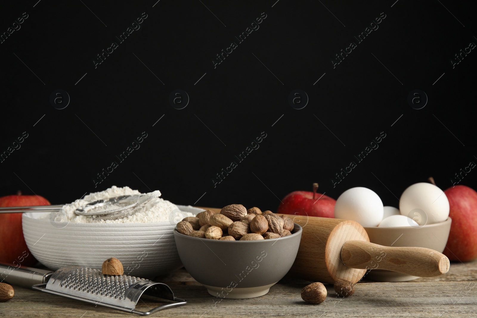 Photo of Nutmeg seeds and other ingredients for pastry on wooden table against black background