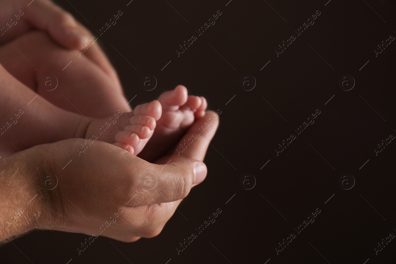 Photo of Father holding his baby against dark background, closeup. Space for text