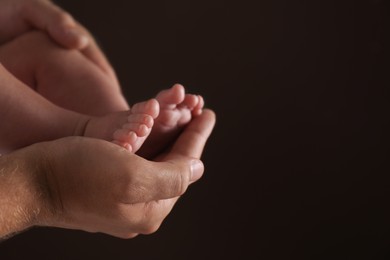 Photo of Father holding his baby against dark background, closeup. Space for text