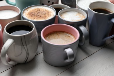 Many different cups with aromatic hot coffee on white wooden table