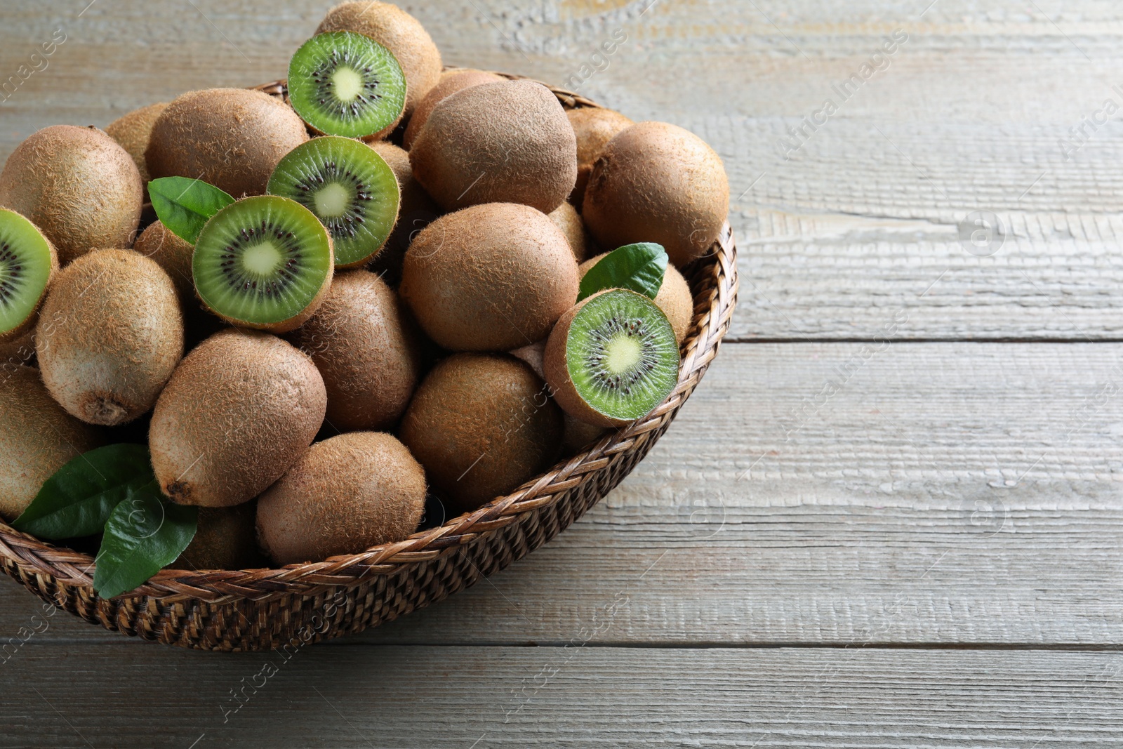 Photo of Fresh ripe kiwis in wicker bowl on wooden table, space for text