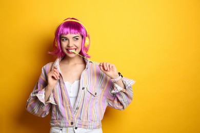 Photo of Fashionable young woman in colorful wig with headphones chewing bubblegum on yellow background, space for text