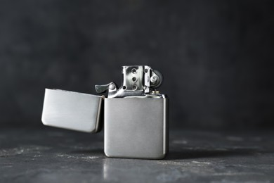 Photo of Metallic cigarette lighter on gray textured table against dark background, closeup