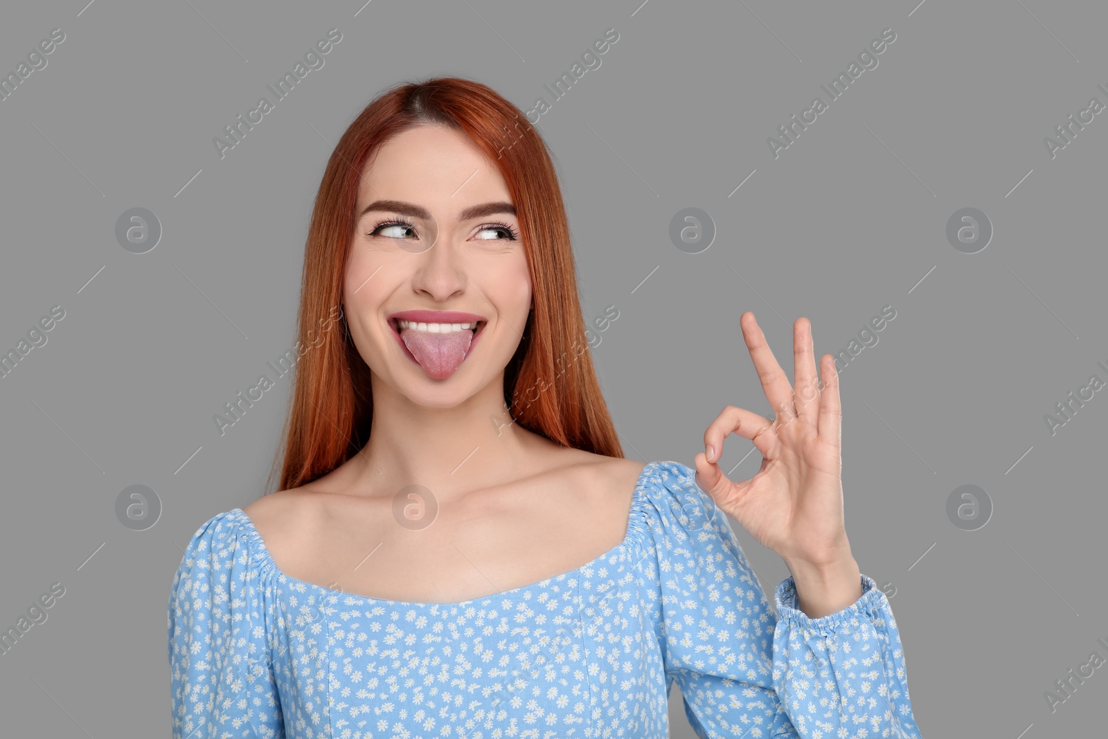 Photo of Happy woman showing her tongue and OK gesture on gray background