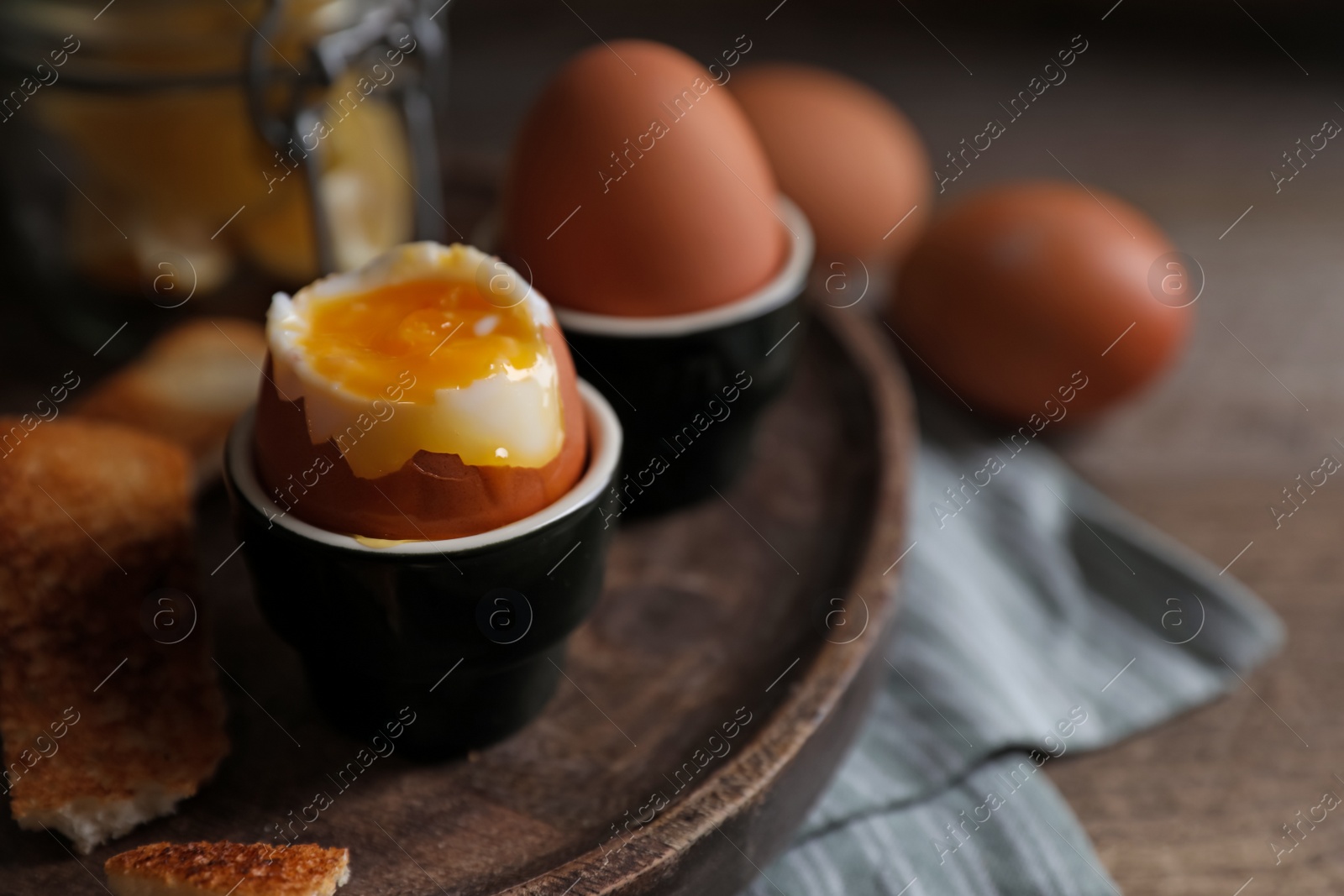 Photo of Tasty boiled eggs in cups on wooden table, closeup