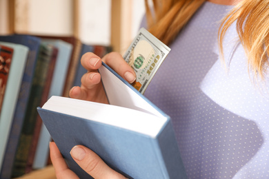 Photo of Woman hiding money in book indoors, closeup. Financial savings