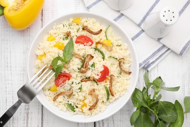 Photo of Bowl of delicious couscous with vegetables and basil served on white wooden table, flat lay