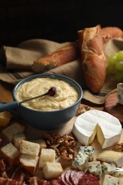 Fondue pot with tasty melted cheese, fork and different snacks on wooden table