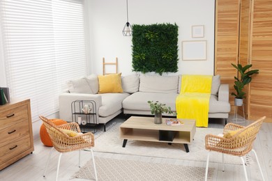 Green artificial plant wall panel and comfortable furniture in cozy living room. Interior design