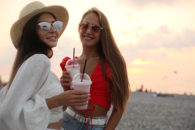 Photo of Beautiful young women with tasty milk shakes on beach