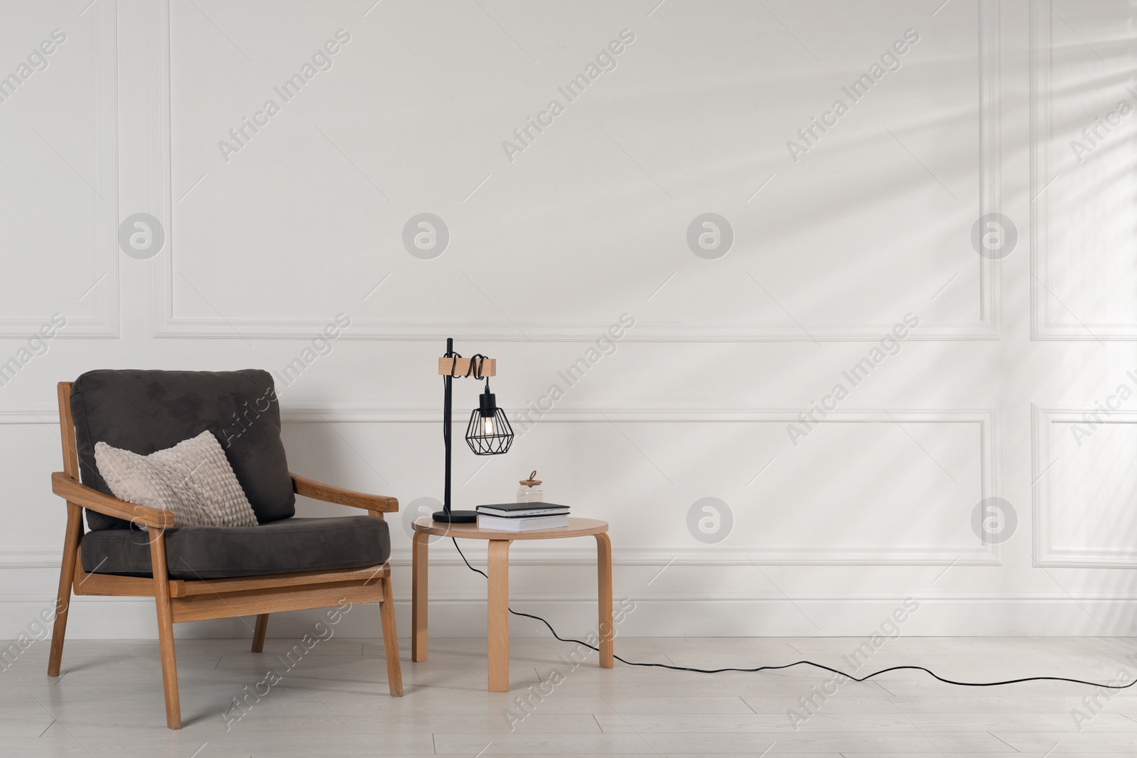 Photo of Comfortable armchair and table with lamp near white wall in room, space for text. Interior design