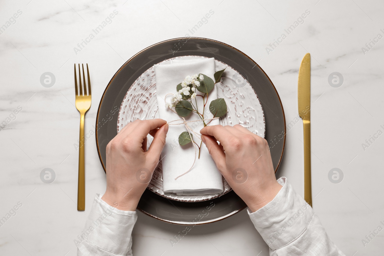 Photo of Woman decorating setting with eucalyptus leaves at white marble table, top view