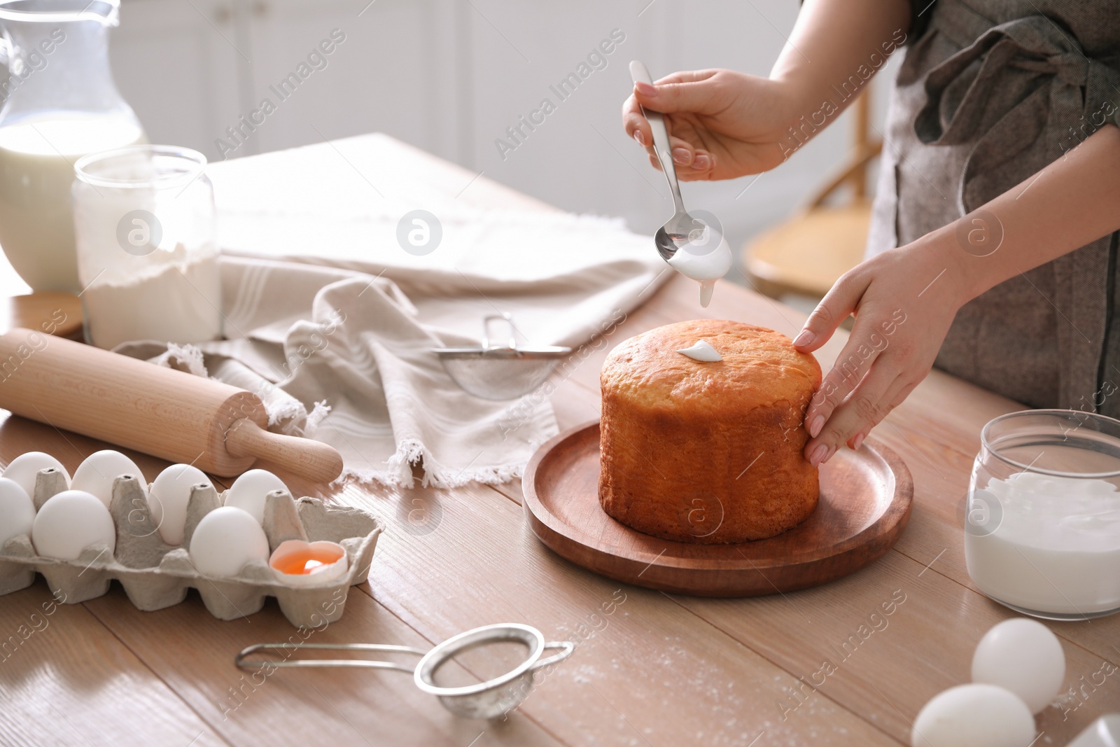 Photo of Young woman decorating traditional Easter cake with glaze in kitchen, closeup