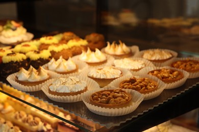 Photo of Different tasty tartlets on counter in bakery shop, closeup. Space for text