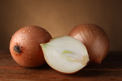 Photo of Whole and cut onions with water drops on wooden table, closeup