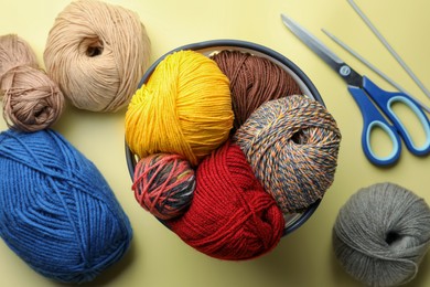 Photo of Soft woolen yarns, knitting needles and scissors on yellow background, flat lay