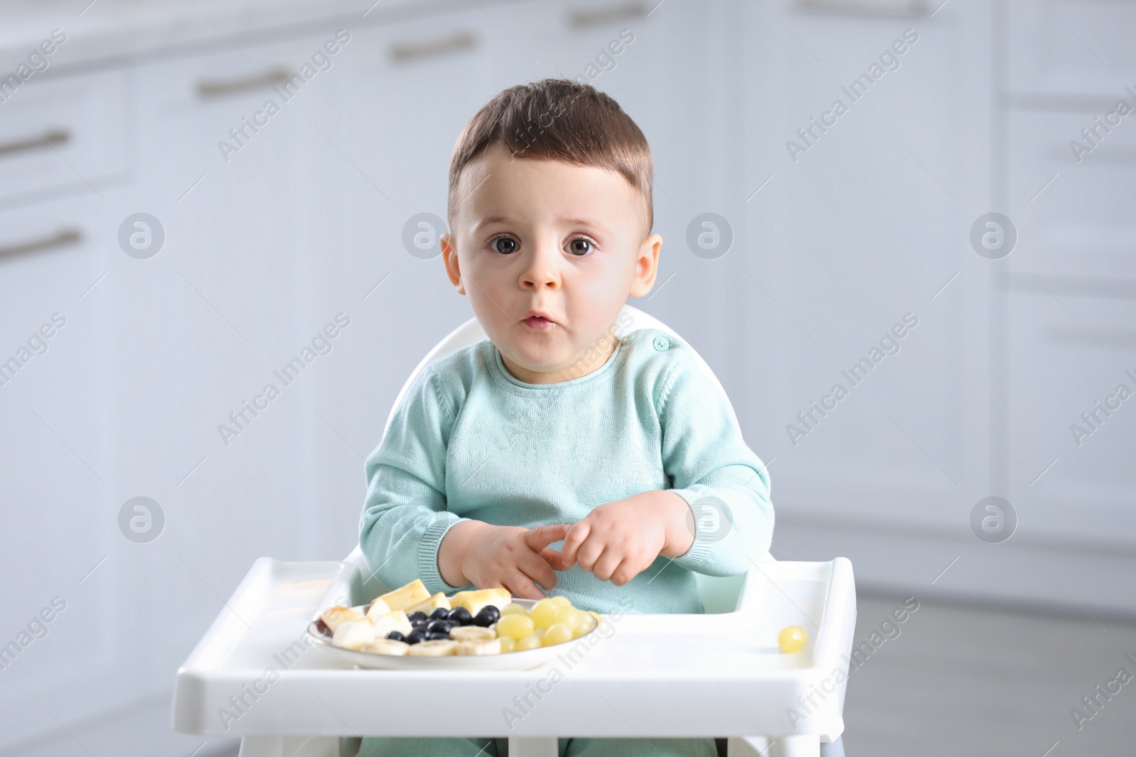 Photo of Cute little baby eating healthy food in high chair at home
