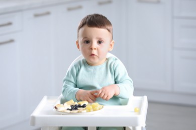 Cute little baby eating healthy food in high chair at home