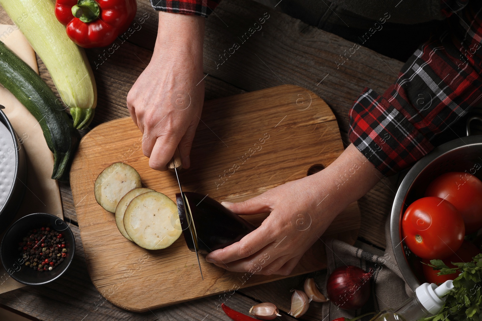 Photo of Cooking delicious ratatouille. Woman cutting fresh eggplant at wooden table, top view