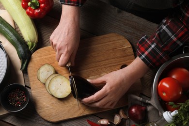 Photo of Cooking delicious ratatouille. Woman cutting fresh eggplant at wooden table, top view