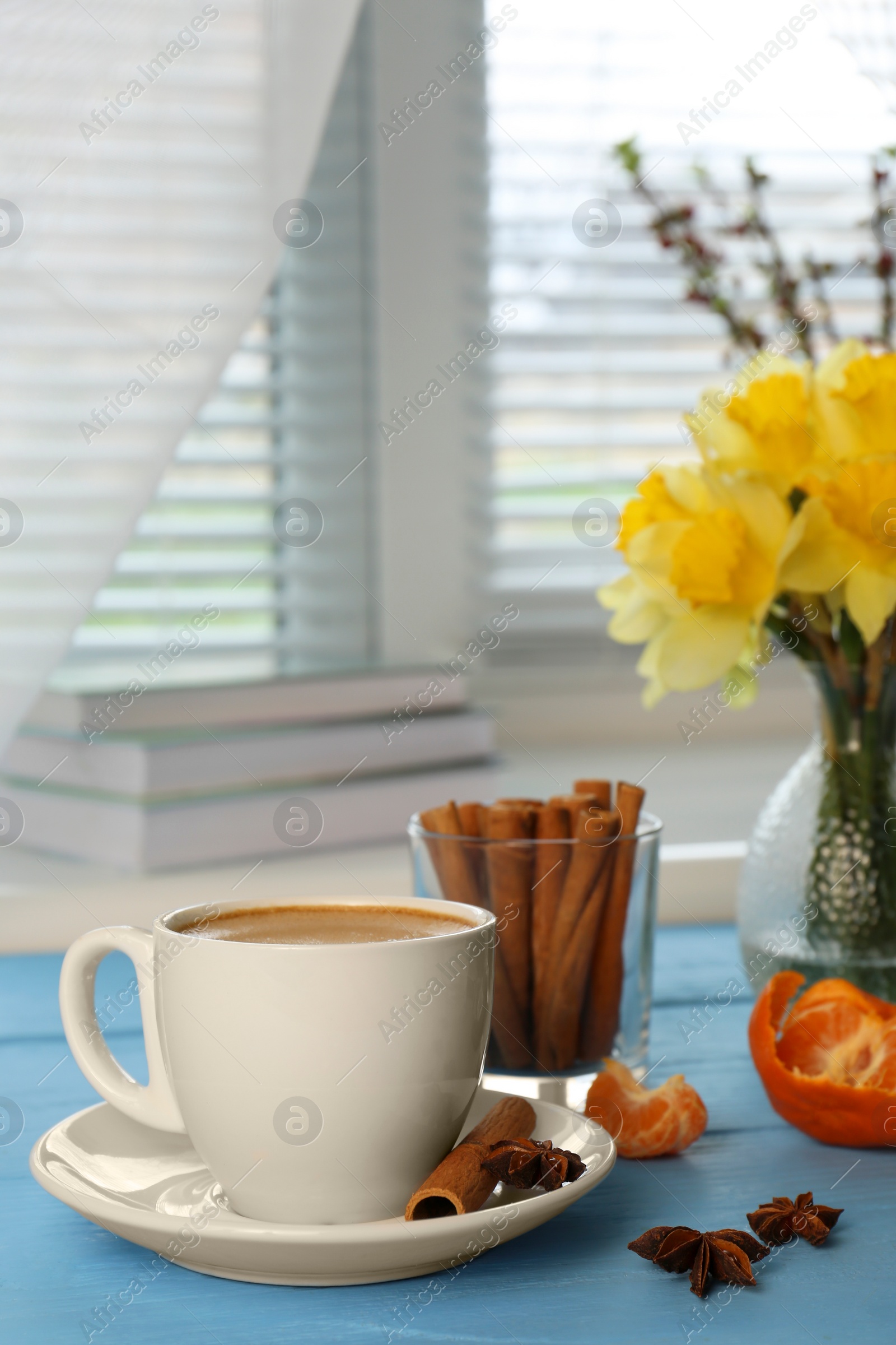 Photo of Cup of coffee, anise stars, yellow daffodils and cinnamon on light blue table