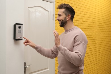 Photo of Happy man ringing intercom while waving to camera in entryway