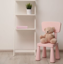 Teddy bear on chair and shelving unit near wall in child room