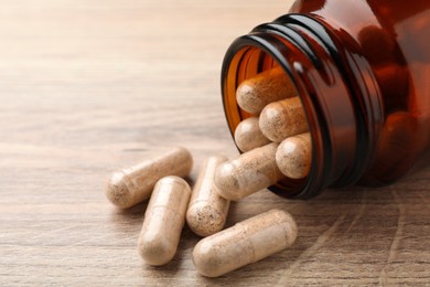 Photo of Gelatin capsules and bottle on wooden table, closeup. Space for text
