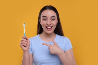 Photo of Happy young woman holding plastic toothbrush on yellow background