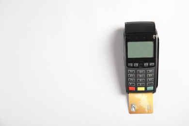 Photo of Modern payment terminal with credit card on white background, top view. Space for text