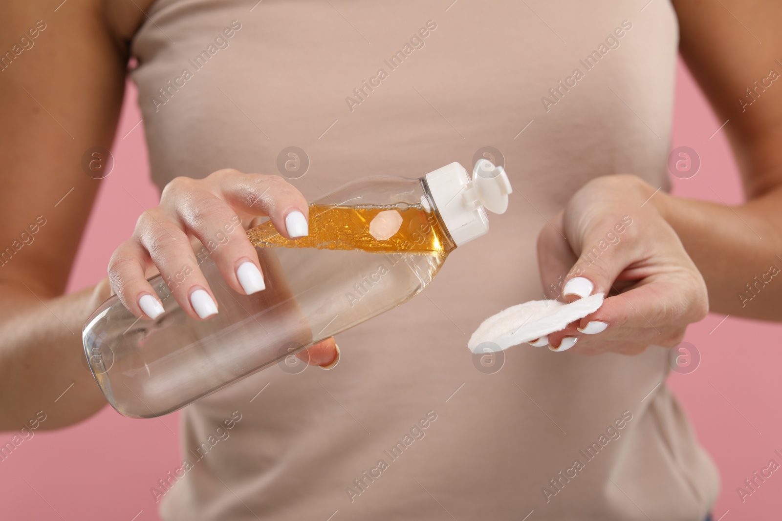 Photo of Woman with makeup remover and cotton pad on pink background, closeup