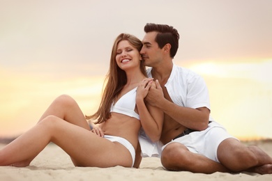 Happy young couple relaxing together on sea beach at sunset