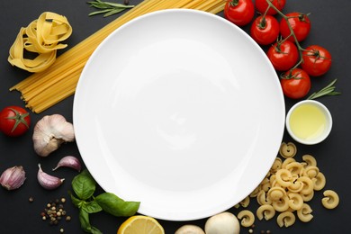 Plate surrounded by different types of pasta, products and peppercorns on black background, flat lay. Space for text