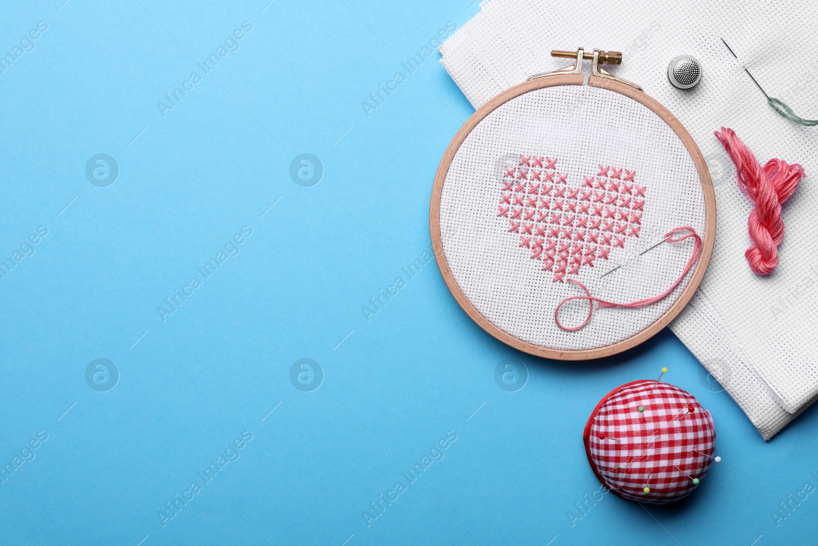 Photo of Flat lay composition with embroidery and different sewing accessories on light blue background. Space for text