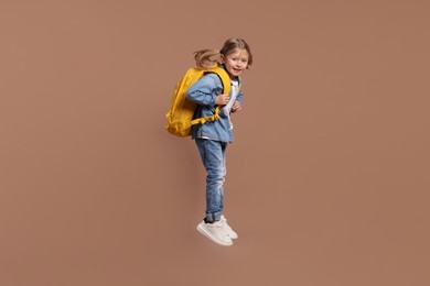 Photo of Happy schoolgirl with backpack jumping on brown background