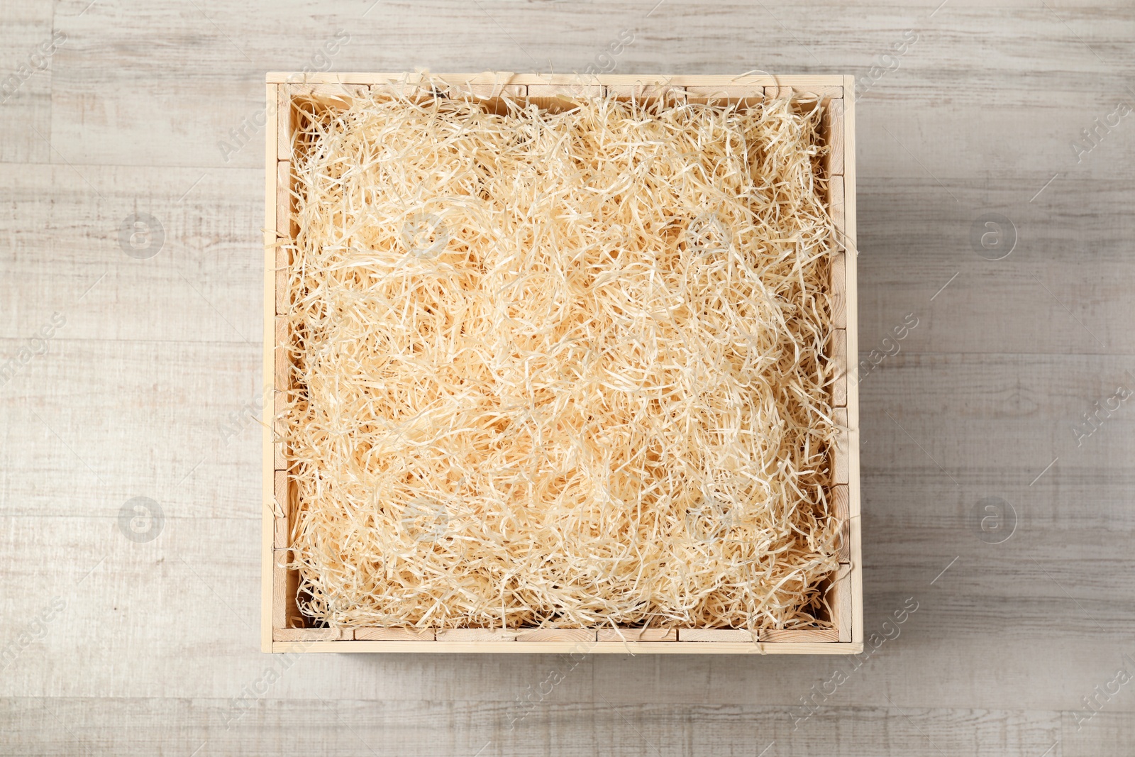 Photo of Wooden crate with filler on light background, top view