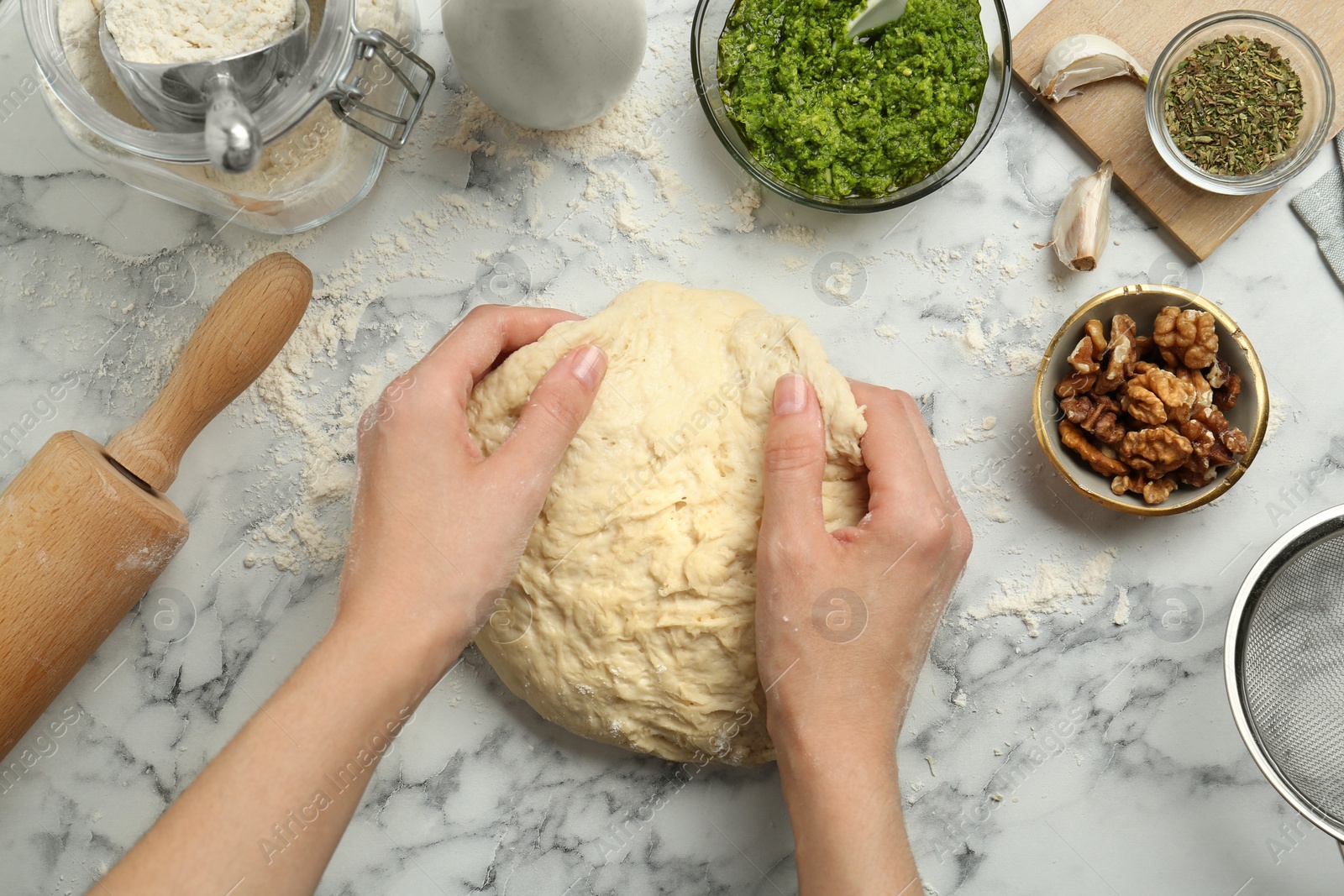 Photo of Woman kneading dough at white marble table, top view. Making delicious pesto bread