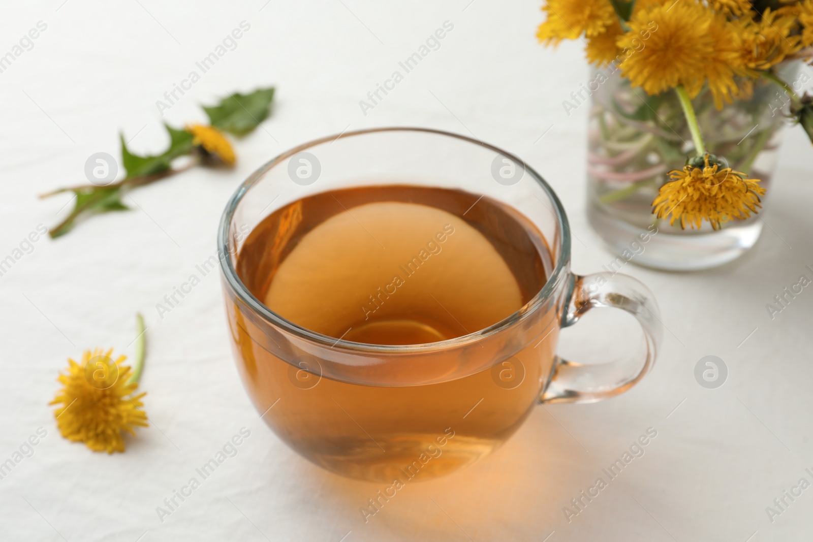 Photo of Delicious fresh tea and beautiful dandelion flowers on white table