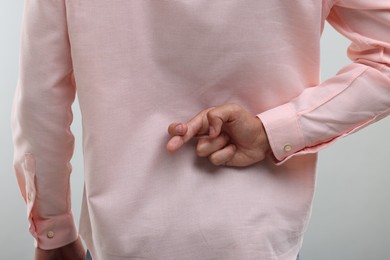 Photo of Young man crossing fingers behind his back on light grey background, closeup