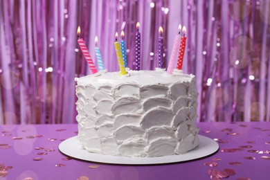 Delicious cake with cream and burning candles on purple background
