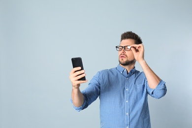 Photo of Man with vision problems using smartphone on grey background