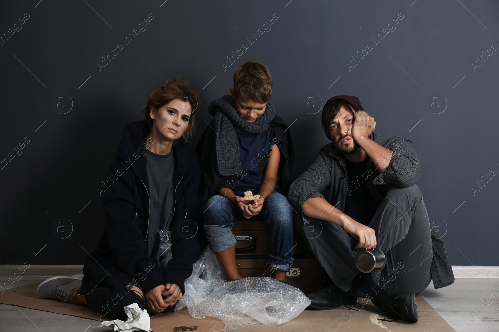 Photo of Poor homeless family sitting on floor near dark wall