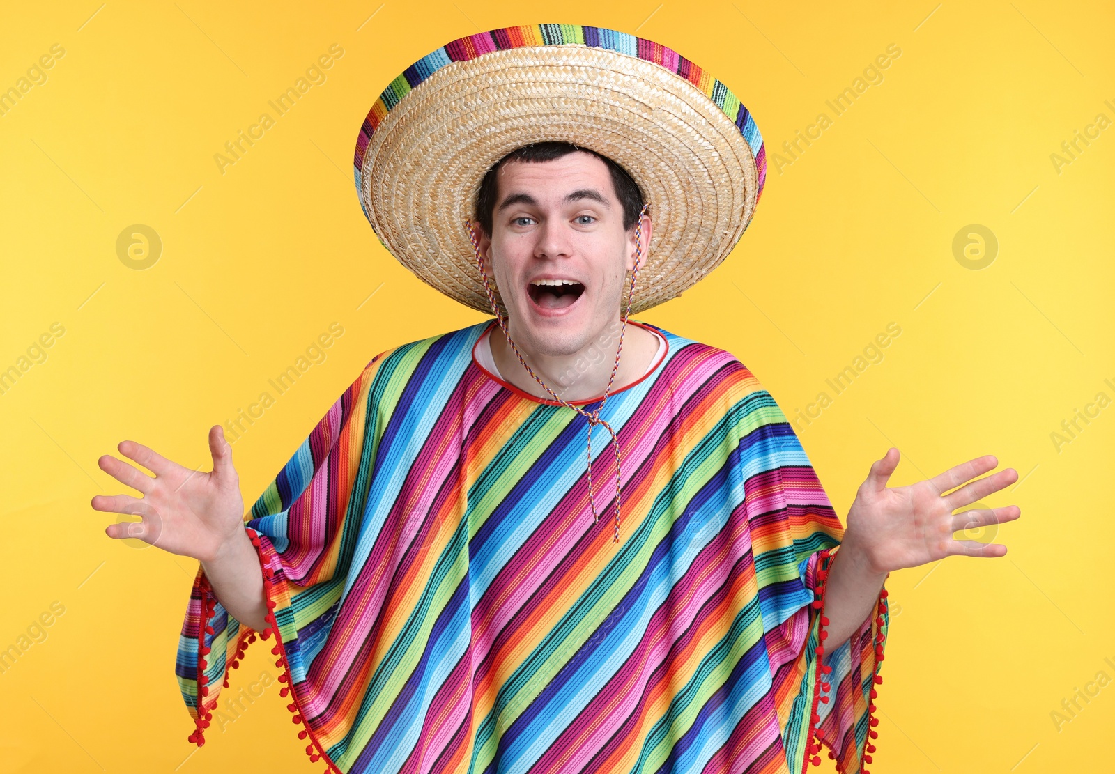 Photo of Excited man in Mexican sombrero hat and poncho on yellow background