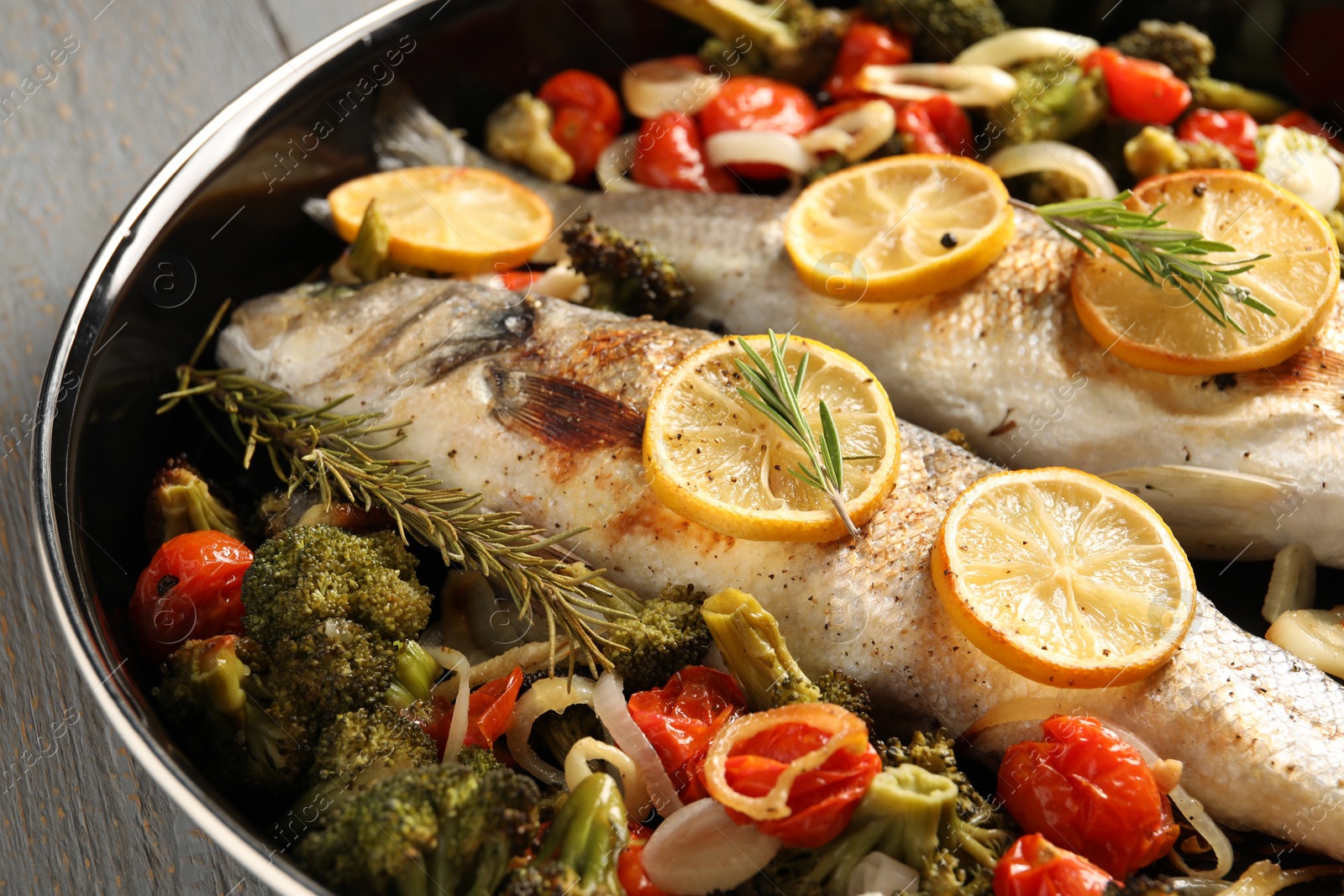 Photo of Baked fish with vegetables, rosemary and lemon on grey wooden table, closeup