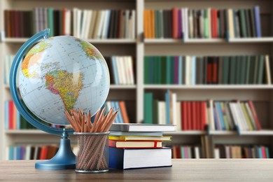 Image of Globe, school supplies and books on wooden table in library. Space for text